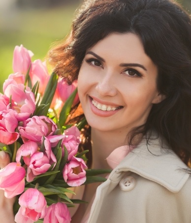 Young woman with clear ceramic braces holding a flower bouquet outdoors