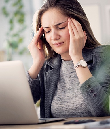 Woman sitting at her computer, suffering from a headache