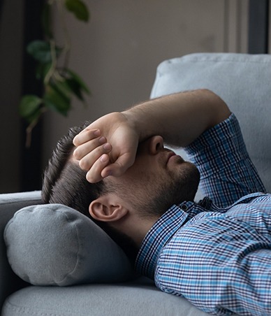 Man lying on sofa, covering his eyes
