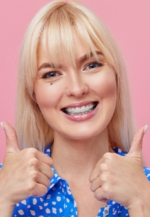 Woman with clear ceramic braces smiling and giving two thumbs up