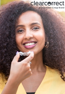 Smiling woman holding a clear aligner