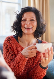 Smiling woman holding a white coffee mug while sitting on couch