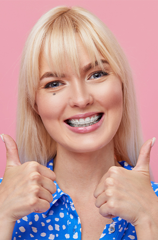 Smiling young woman with clear ceramic braces giving two thumbs up