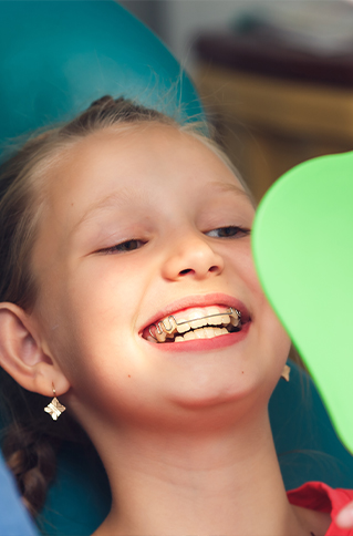 Young girl with braces looking at her teeth in mirror