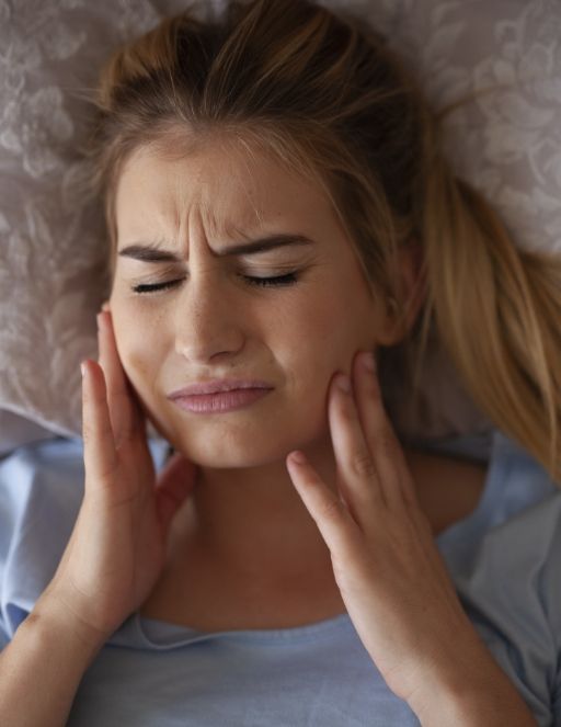 Woman laying in bed touching her jaw in pain