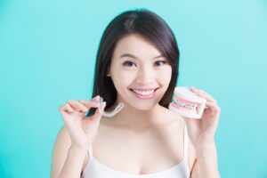 Woman holding clear aligner and dental model with braces